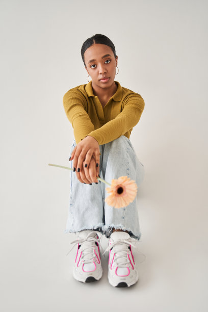 严肃细心的女人坐在镜头前的地板上，手里拿着温柔的花图片下载