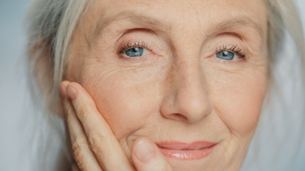特写肖像美丽的高级妇女轻轻应用面霜。老年妇女使她的皮肤柔软，光滑，皱纹与天然抗衰老化妆品。美容护肤品图片下载