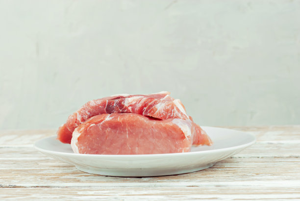 白色盘子里的红肉收起来。白色背景上的一块猪肉。准备肉类菜肴。复制空间和食物附近文本的自由空间。图片下载