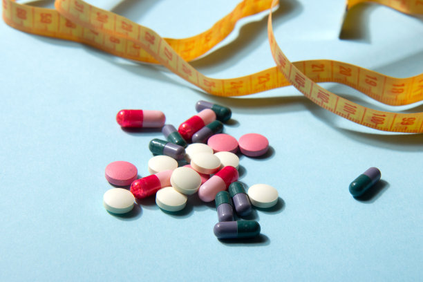 维生素片和胶囊，以及蓝色背景上亮黄色的卷尺。膳食补充剂图片下载