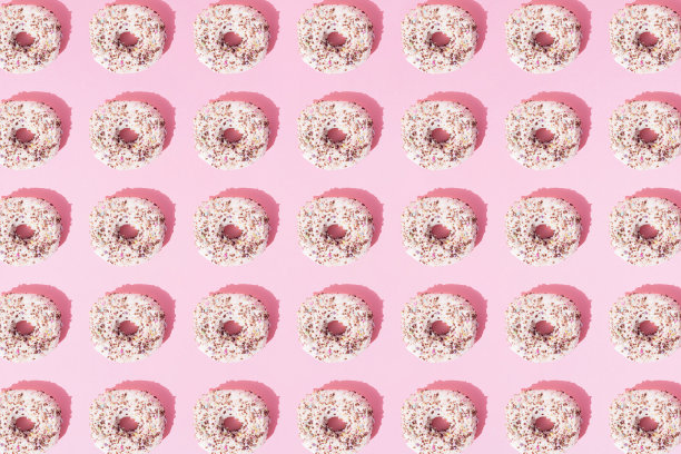 在粉红色的粉彩背景上布置白色的小甜甜圈和彩色的面包屑。模式。平的。图片下载