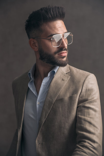 英俊的胡子男人的肖像在米色西装与眼镜看向一边图片下载
