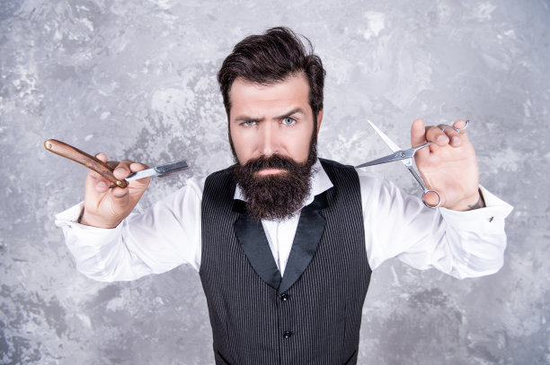 英俊野蛮的男人理发师与胡子持有理发店复古剃须刀刀片和剪刀，发廊。图片下载