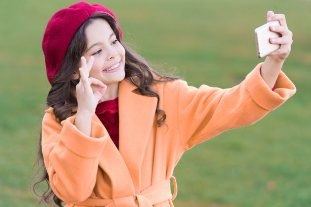 完美的照片。智能手机的应用程序。现代通信。女孩拿着手机自拍。社交网络自拍。在线直播或拍摄视频日志。小女孩手持智能手机图片下载