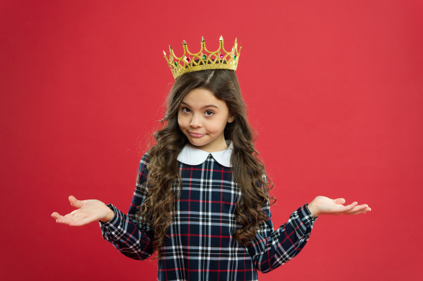 世界在我身边旋转。孩子戴着象征公主的金色皇冠。每个女孩都梦想成为公主。女士小公主。女孩戴着红色背景的皇冠。被宠坏的孩子的概念。自我中心的公主图片下载