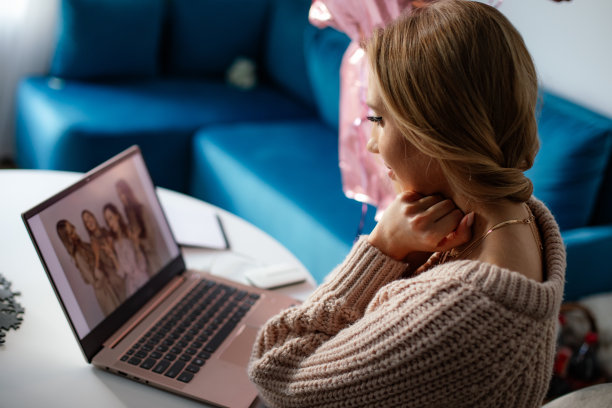 年轻的金发微笑的女人的肖像看着朋友的照片从笔记本电脑在家里的生日。远程的节日图片下载