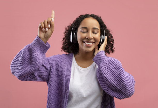 年轻漂亮的黑人女子戴着无线耳机听着音乐，闭上眼睛，手指向上图片下载