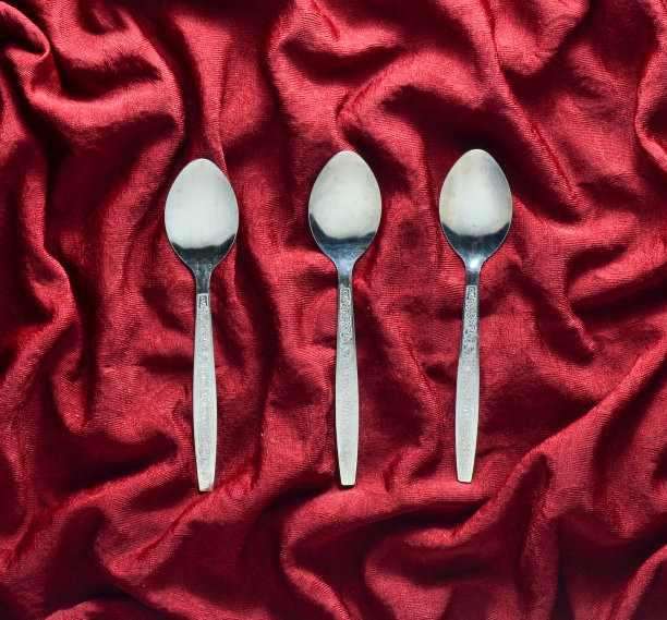 一套三个金属勺子放在红色丝绸桌布上。前视图。图片下载