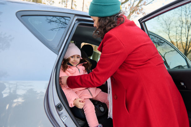 一个慈祥的妈妈系着她可爱的小女儿的安全带的后视镜。儿童在车中的安全运动，汽车的安全保障和安全乘车的概念。图片下载