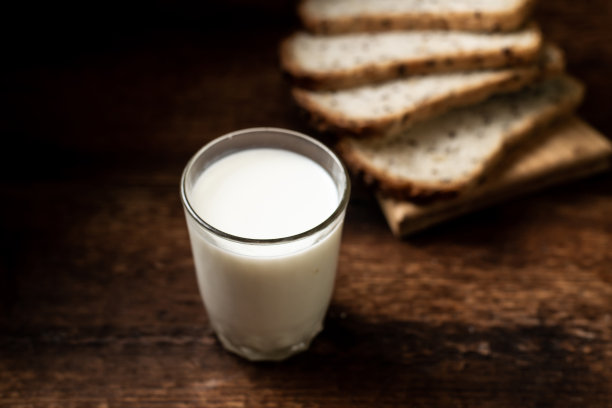 一杯牛奶。背景中的面包是模糊的。深色木制背景。早上的早餐。乡村风格图片下载