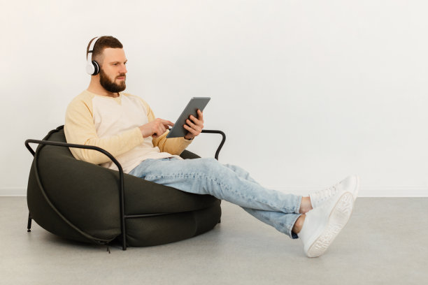 严肃的家伙使用平板电脑，戴着耳机坐在室内，侧视图片下载