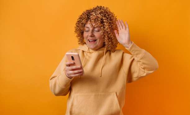 近距离的肖像的一个有吸引力的年轻的30多岁的女人与非洲式卷发有高兴的表情使用智能手机孤立在黄色的墙壁背景图片下载