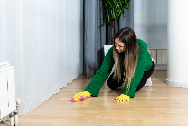 有吸引力的白人妇女跪在地板上，用抹布擦它，享受清洁她的家。一个戴着黄色橡胶手套的女人在擦拭公寓的地板。图片下载