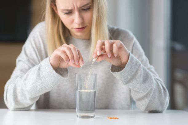 年轻漂亮的病人坐在桌子旁，吃药，把药放在一杯水中止痛图片下载