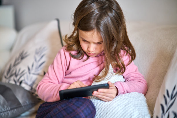 一个小女孩坐在沙发上玩手机图片下载