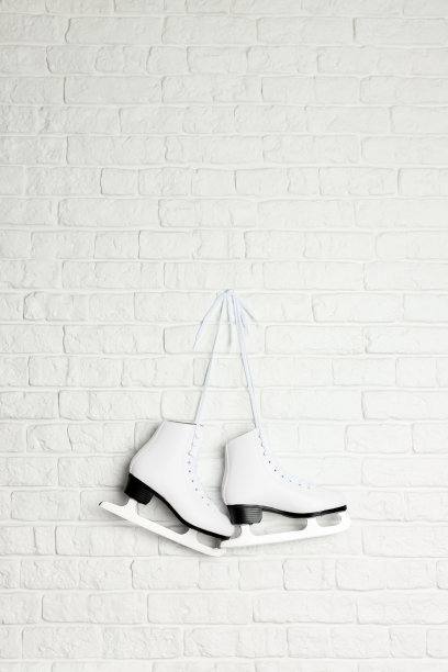 白色的冰上花样滑冰鞋挂在砖墙上。图片下载