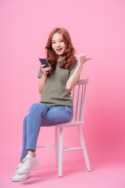 年轻的亚洲妇女坐在和使用粉红色背景的智能手机图片下载