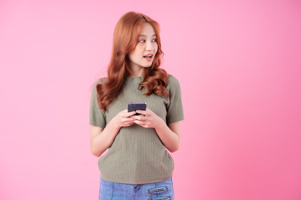 年轻的亚洲女性使用粉色背景的智能手机图片下载