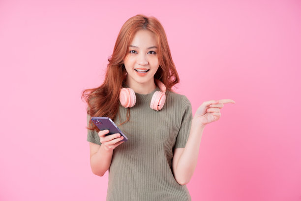 年轻的亚洲女性使用智能手机，以粉色为背景听音乐图片下载