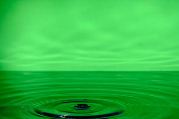 明亮的绿色背景与发散的圆圈从水滴表面的水。图片下载