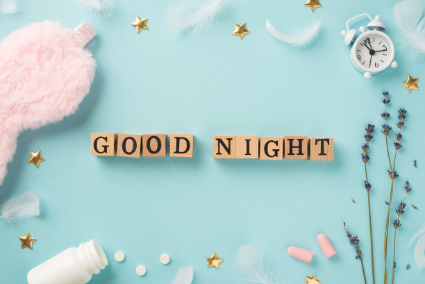 俯视图照片木制立方体晚安文本薰衣草白色闹钟粉红色蓬松睡眠面具耳塞开瓶与药丸羽毛和金色星星在孤立的淡蓝色背景图片下载