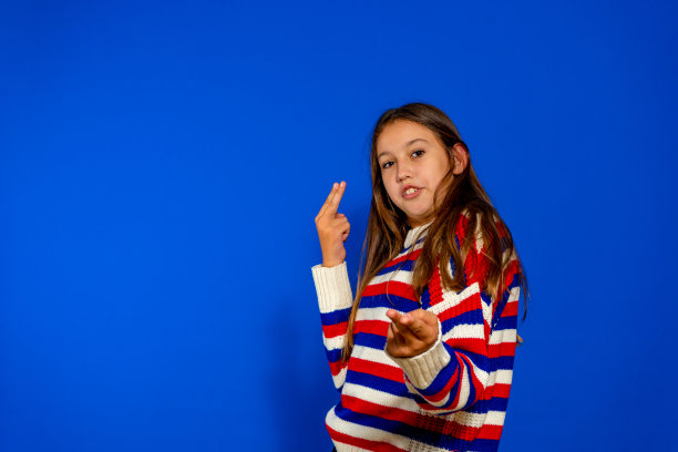 肖像图像非常高兴，惊讶，微笑的黑发女孩在条纹毛衣显示有趣的手势与手，孤立在蓝色背景与复制空间。图片下载