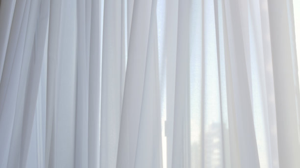 从较低的角度，你可以看到窗户上透明的白色窗帘是如何随着窗帘平滑地吹起美丽的波浪。薄纱项链轻轻摆动图片下载
