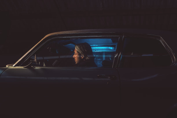 一个金发男人晚上坐在一辆美国经典肌肉车里。图片下载