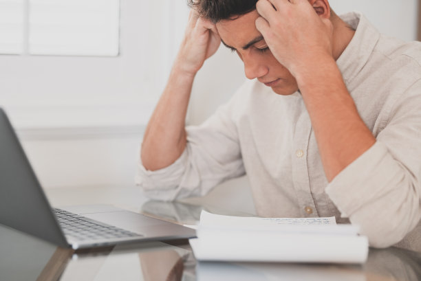 由于过度劳累和为考试而努力学习，精神紧张的年轻人在家饱受头痛之苦。疲惫的男青少年在做学校作业图片下载