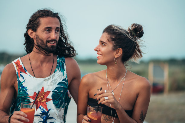 迷人的年轻夫妇带着酒精鸡尾酒在海滩上散步图片下载