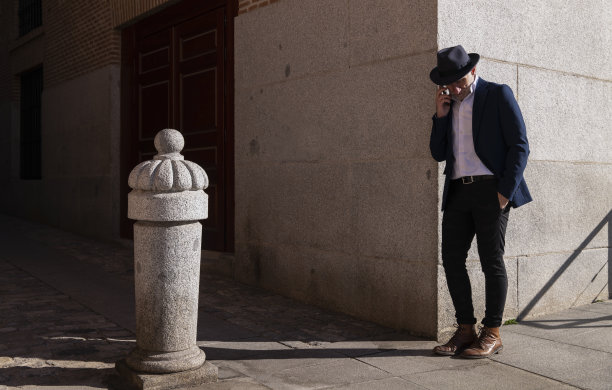 身长成人男子，戴着帽子和西装，靠墙在街上拿着手机。马德里,西班牙图片下载