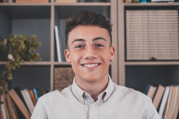 肖像的一个年轻和快乐的开朗的人微笑着看着相机有乐趣。男性在家办公的大头照。图片下载