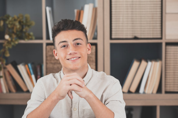 一名年轻快乐的男子微笑着看着相机享受乐趣的肖像。男性在办公室工作的头部照片。图片下载