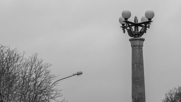 一盏巨大的旧街灯的黑白照片，背景是冬天灰色的天空。图片下载