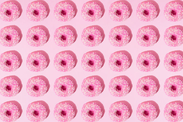 在粉红色粉彩的背景上，用釉料和白色碎屑排列粉红色的环形甜甜圈。模式。平的。图片下载