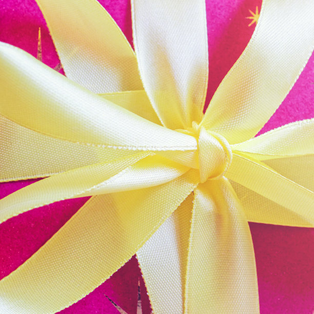 一个黄色缎带蝴蝶结系在一个礼物包装在纸上。节日背景(生日、婚礼、圣诞节、周年纪念等)。图片下载