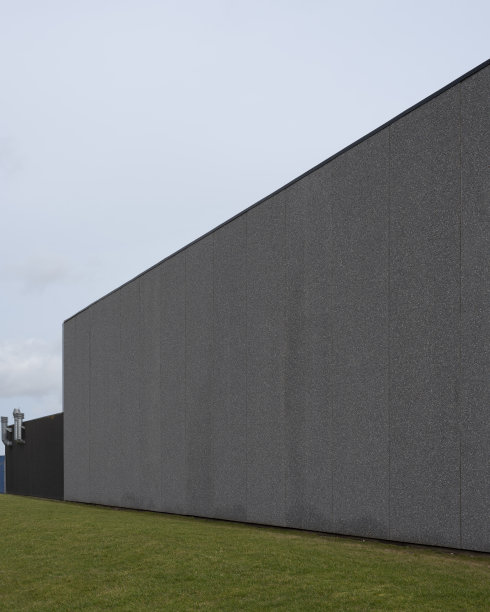 在灰色混凝土的仓库建筑上有一面灰色的空墙，前景是一片草坪图片下载