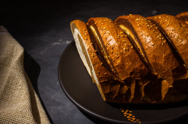 不寻常的两色新鲜面包在陶瓷盘子和编织餐巾在黑色的背景上，照片在强光下低调，特写。图片下载