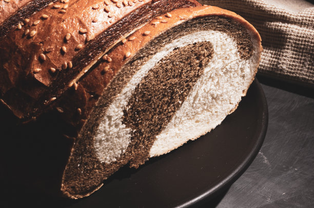 不寻常的两色新鲜面包在陶瓷盘子和编织餐巾在黑色的背景上，照片在强光下低调，特写。图片下载