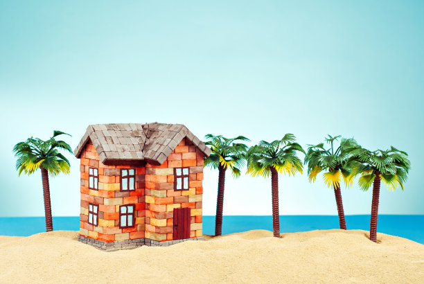 在沙滩上模拟一座房子。以大海和蓝天为背景的海滨别墅。买房和抵押贷款的概念。房子附近有棕榈树和天堂岛。图片下载