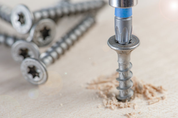 把螺钉拧进单板。家具生产时，一把螺丝刀将一颗自攻螺钉拧成一块板。桌面上放着几颗银螺丝钉图片下载