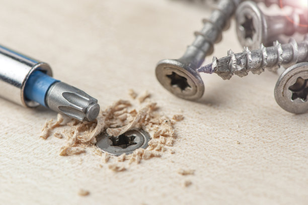 把螺钉拧进单板。家具生产时，一把螺丝刀将一颗自攻螺钉拧成一块板。桌面上放着几颗银螺丝钉图片下载