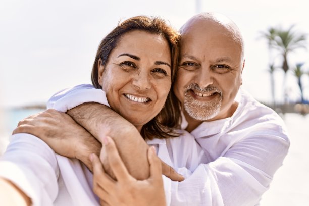 在一个阳光明媚的日子里，一对中年西班牙夫妇在海滩上散步。拥抱在爱的假期去海边拍一张自拍图片下载