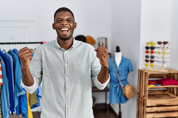 年轻的非洲裔美国人在零售精品店担任经理，兴奋地举起双臂，闭上眼睛，微笑着庆祝胜利。赢家的概念。图片下载