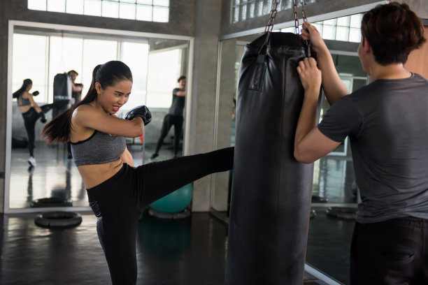拳击女子在体育馆踢教练拿的沙袋图片下载