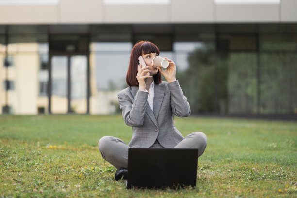 商业女性坐在城市公园的草地上用现代智能手机聊天图片下载