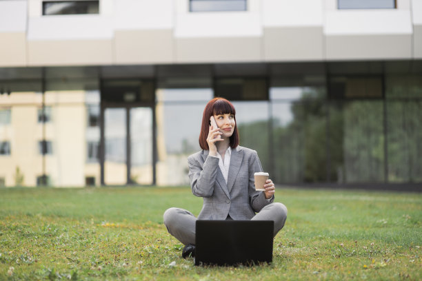 商业女性坐在城市公园的草地上用现代智能手机聊天图片下载