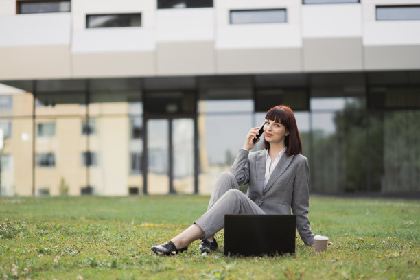 这张照片拍摄的是一名穿着职业装的白人女性坐在城市公园的草地上图片下载
