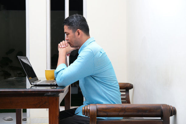 侧面的成人亚洲人看着笔记本电脑严肃的表情，而坐在他的房子图片下载