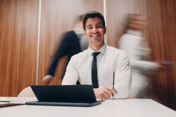 使用笔记本电脑的商人坐在办公室会议的桌子旁，与走动的人的运动模糊的背景。商务人士男女小组会议讨论图片下载